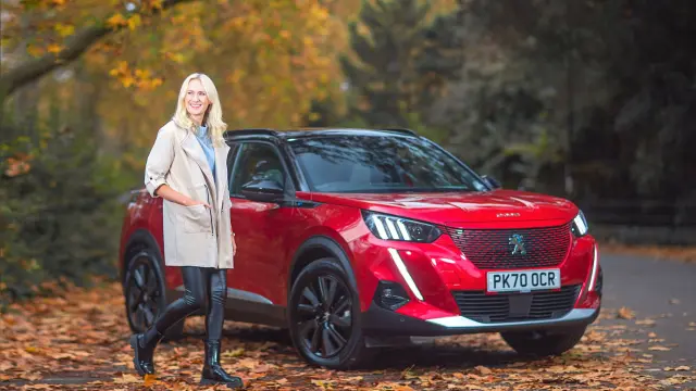 Woman standing next to a red Peugeot e-2008 with an autumnal backdrop